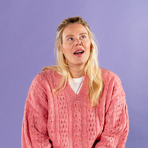 Business student Chantelle Reese wearing pink jumper sat in front of purple backdrop