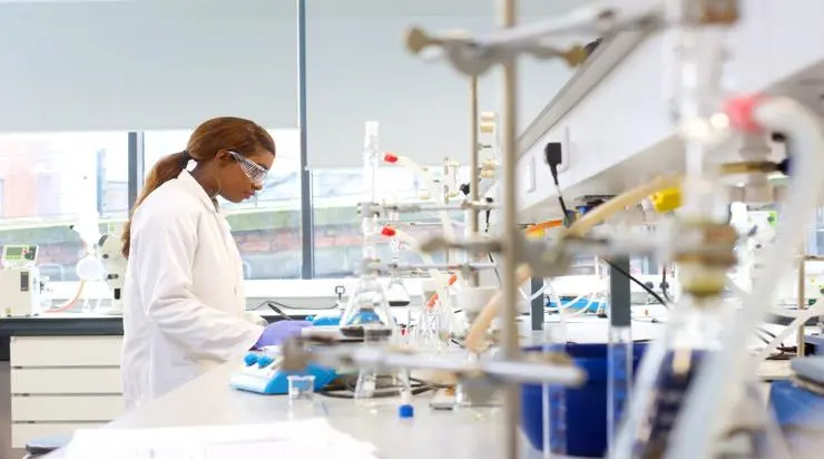 Student in a white lab coat performing a chemistry experiment in the lab