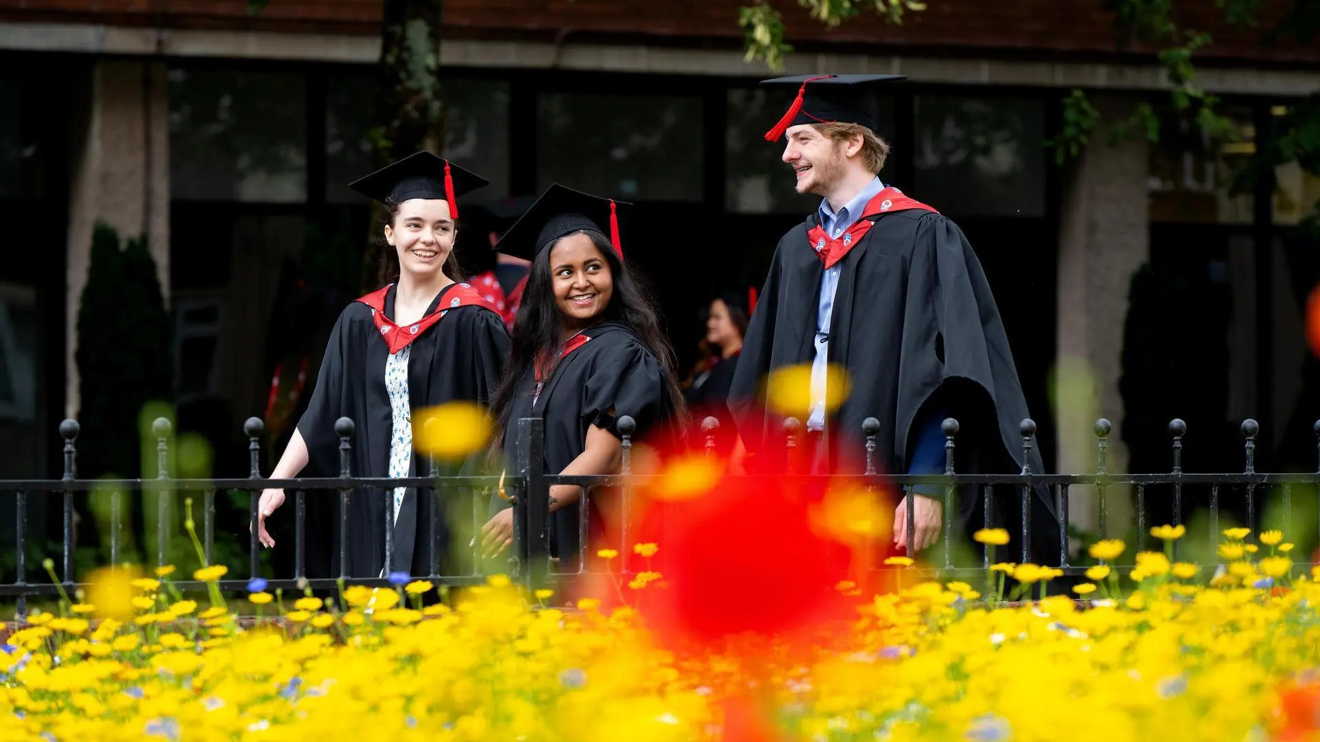 A group of graduates walk together in front of a patch of flowers.