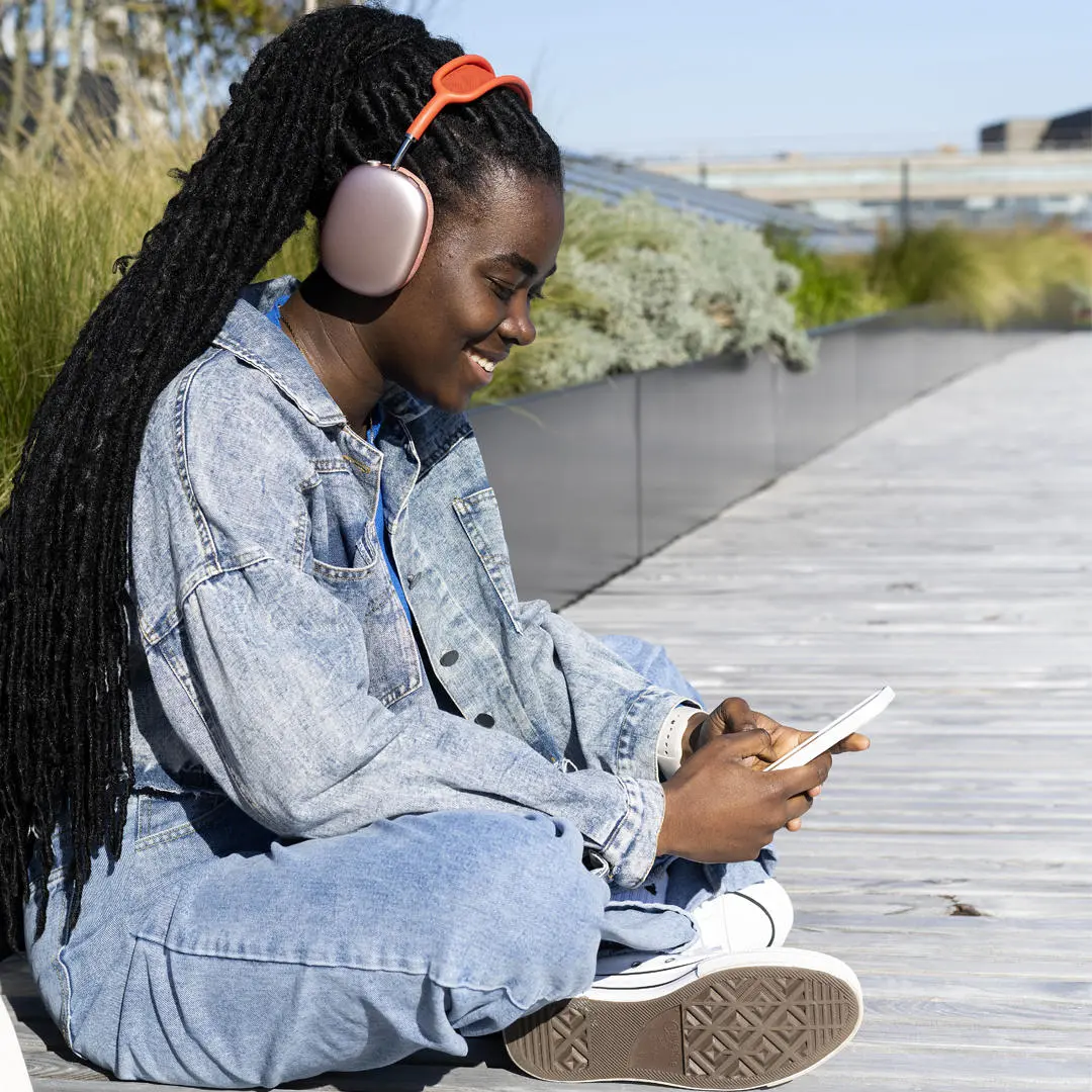student wearing denim and headphones looking at a phone on the student centre roof