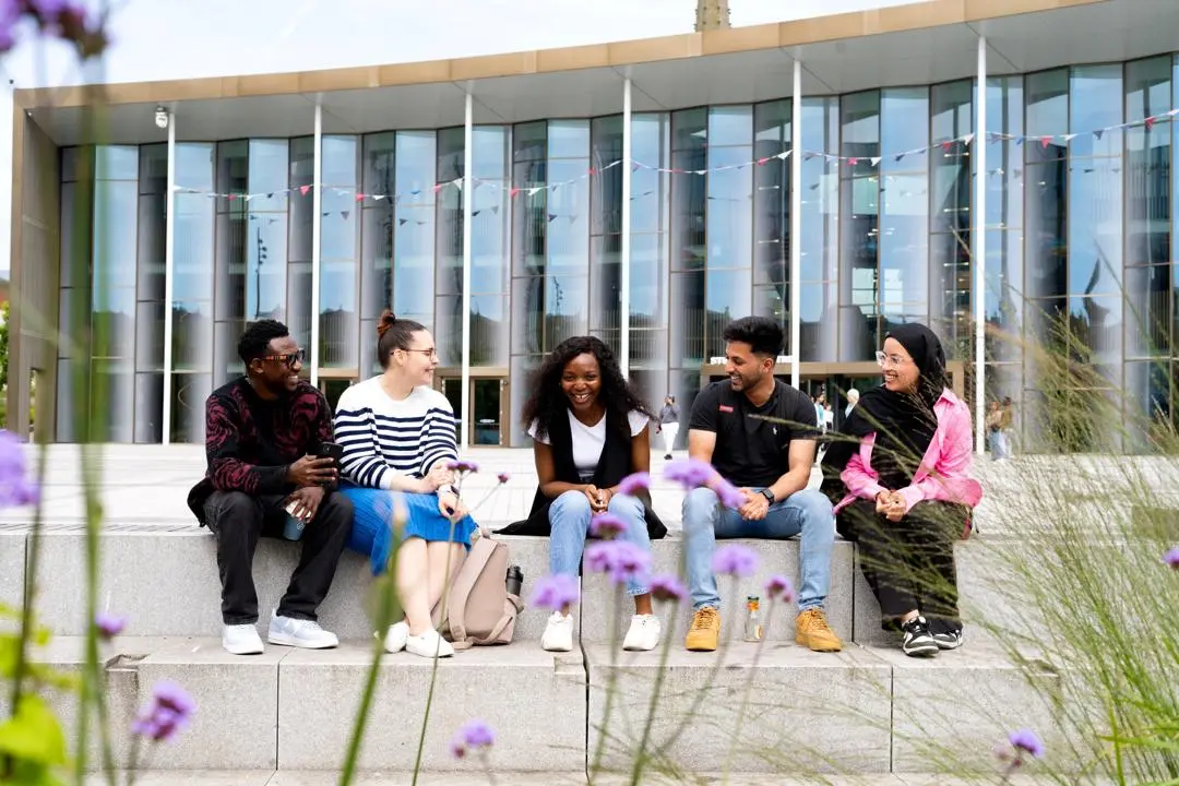 Group of students sitting on the steps outside the front of the student centre