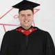 UCLan Partner graduate Adam Lever smiles, wearing a cap and gown on their graduation day.