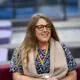 harriet tyler from the people team sat on a burgundy sofa with a blue leopard print top on, glasses and a rainbow lanyard