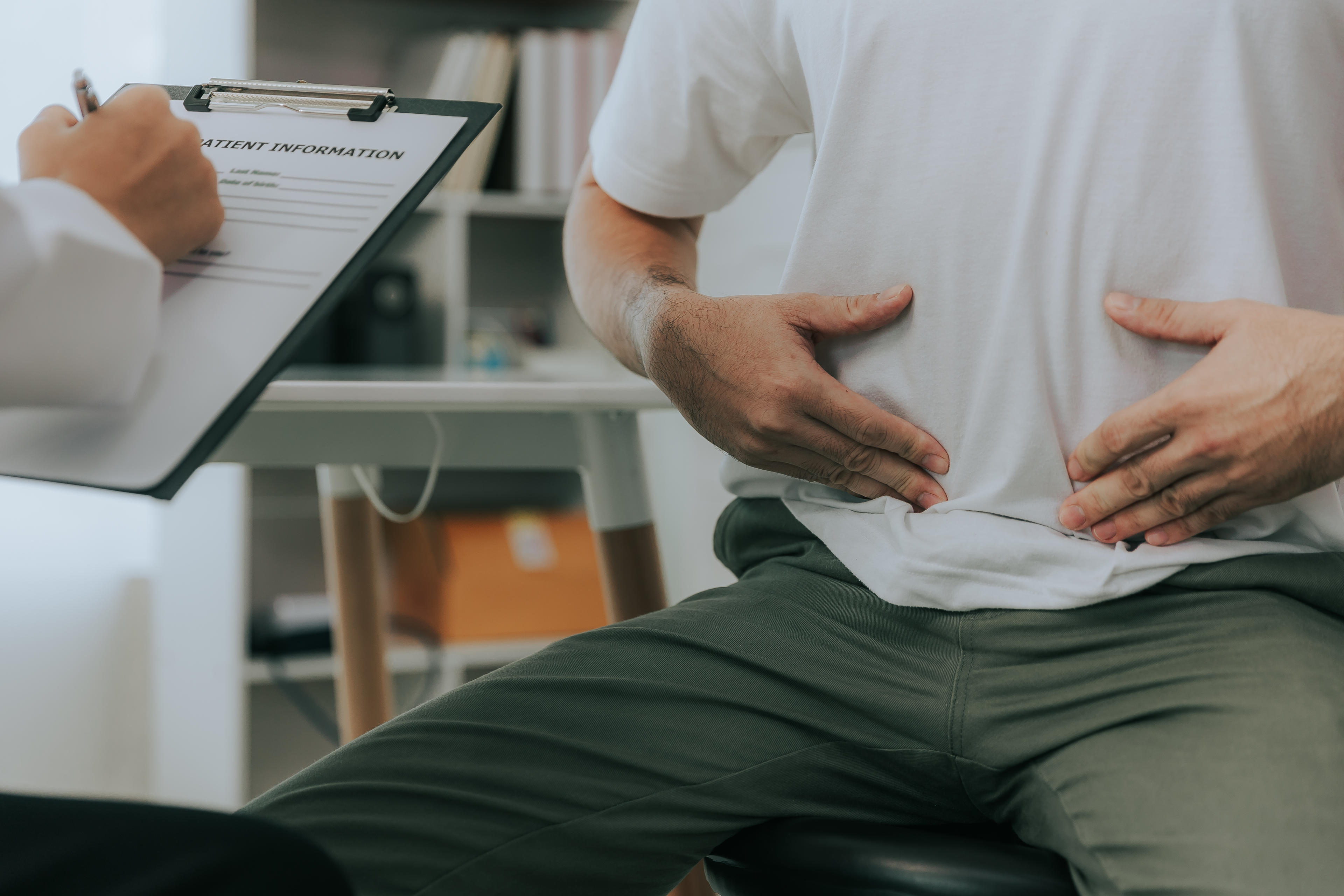 Stock image showing Doctor counselling male patient with abdominal pain in hospital examination room