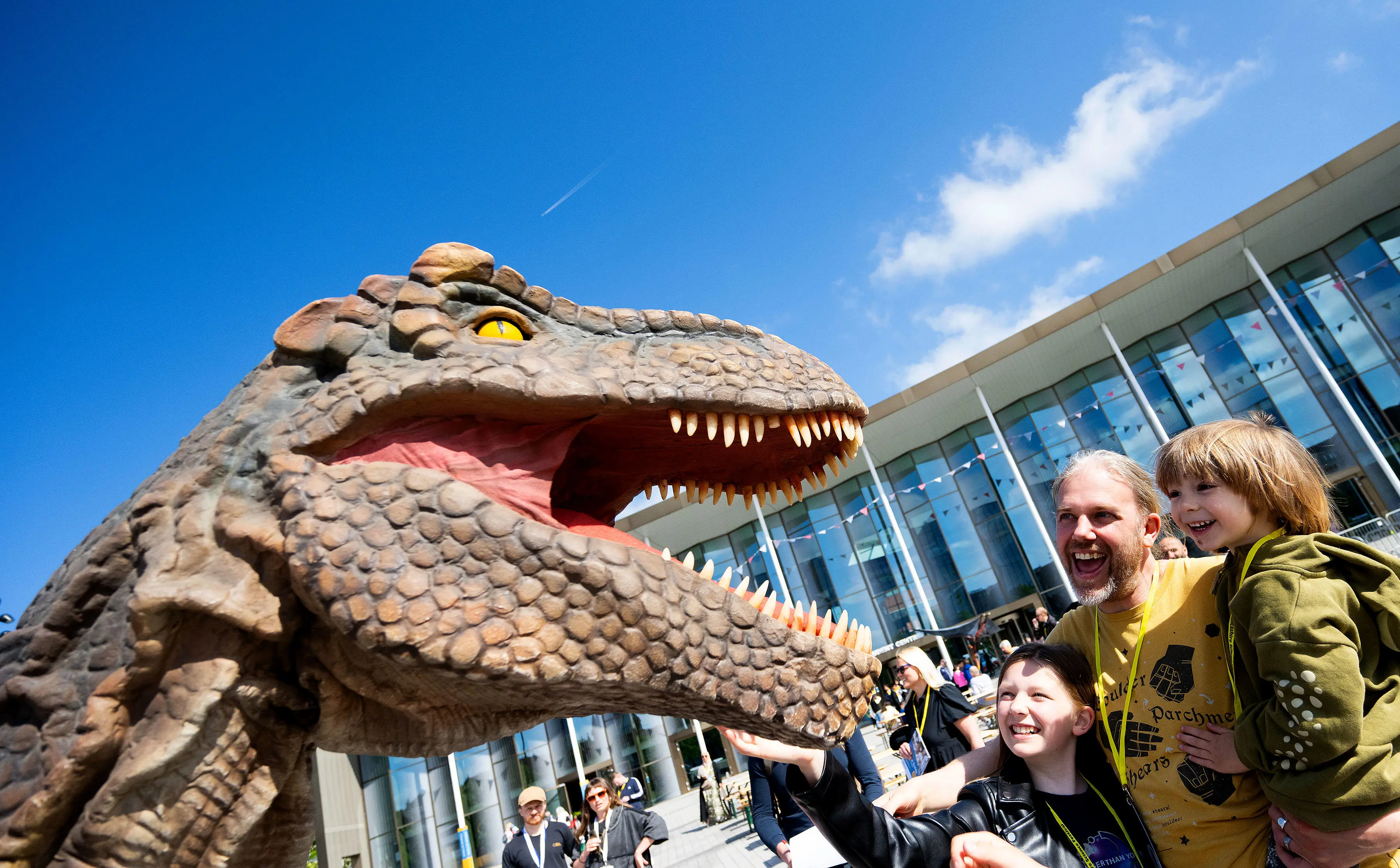 Man with two children looking into the mouth of a huge model dinosaur