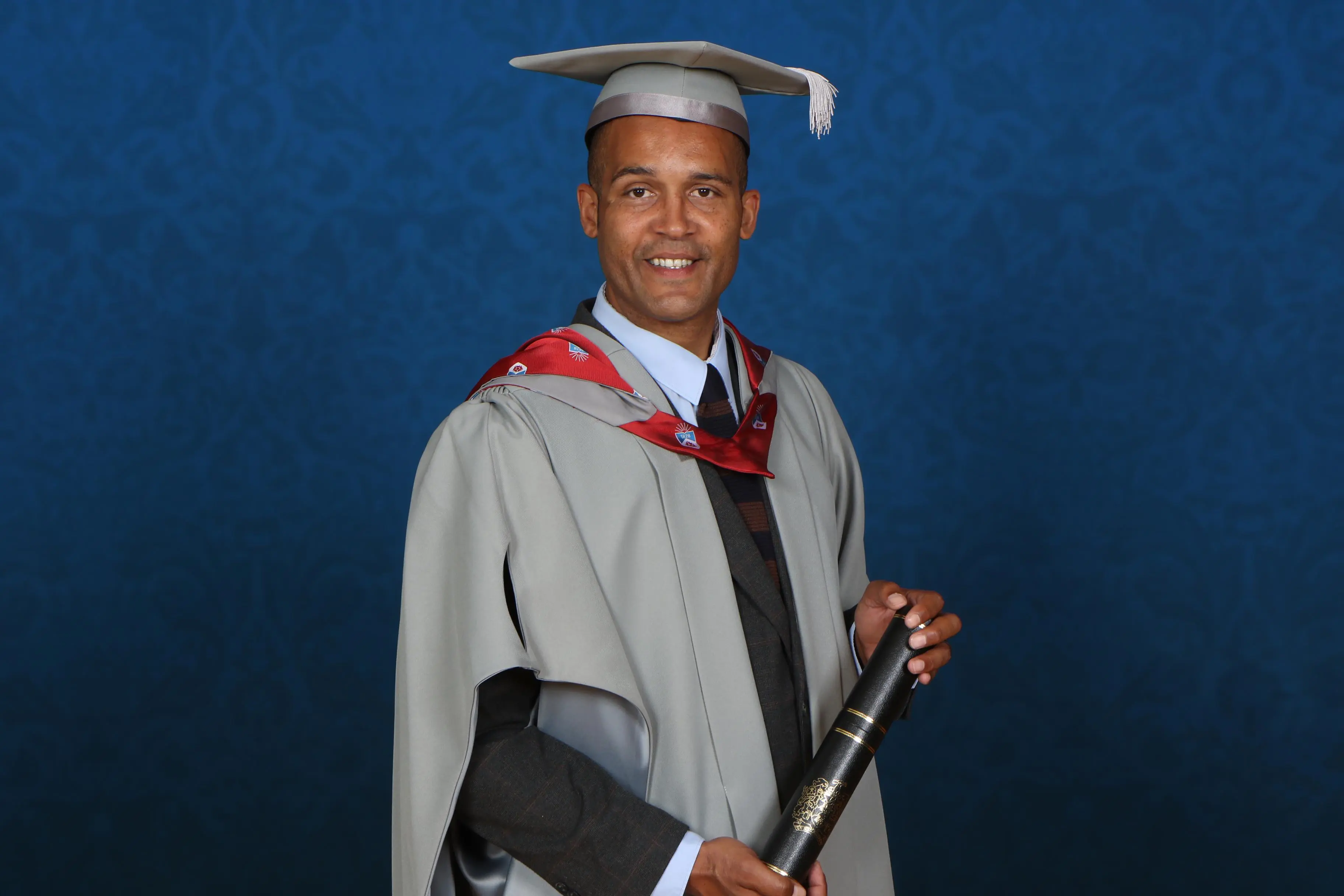 Clarke Carlisle dressed in academic robes and holding a scroll