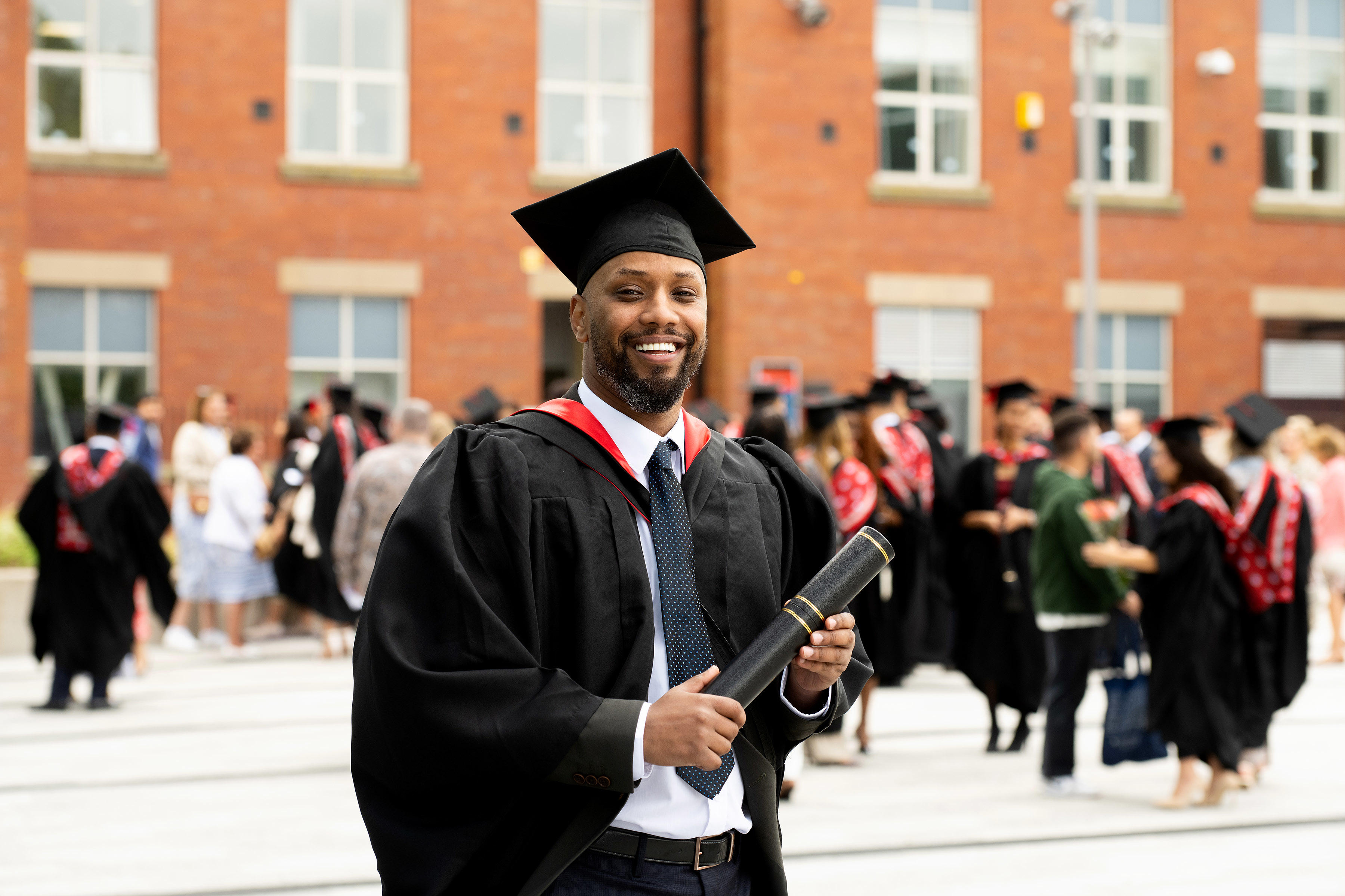Hamza Hussan dressed in academic robe and holding a scroll
