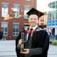 Ian Buckman dressed in a cap and gown and holding a scroll